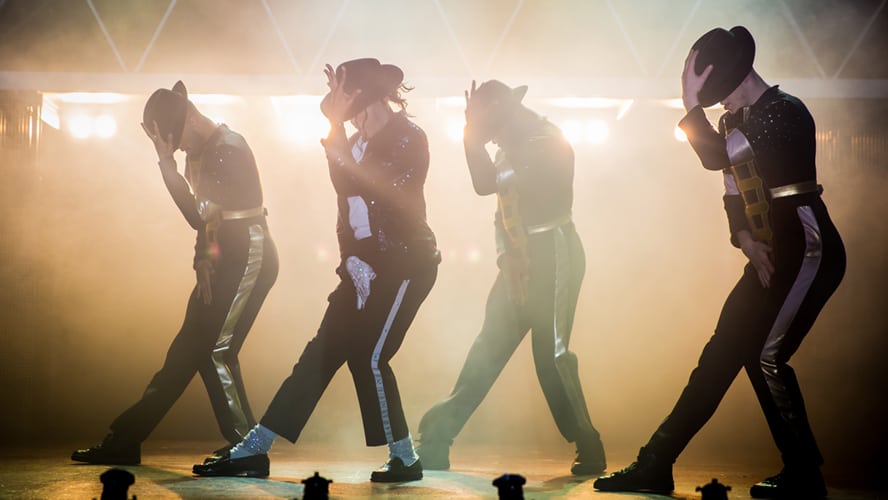 A vibrant stage scene featuring dancers in dynamic poses, illuminated by colourful spotlights.