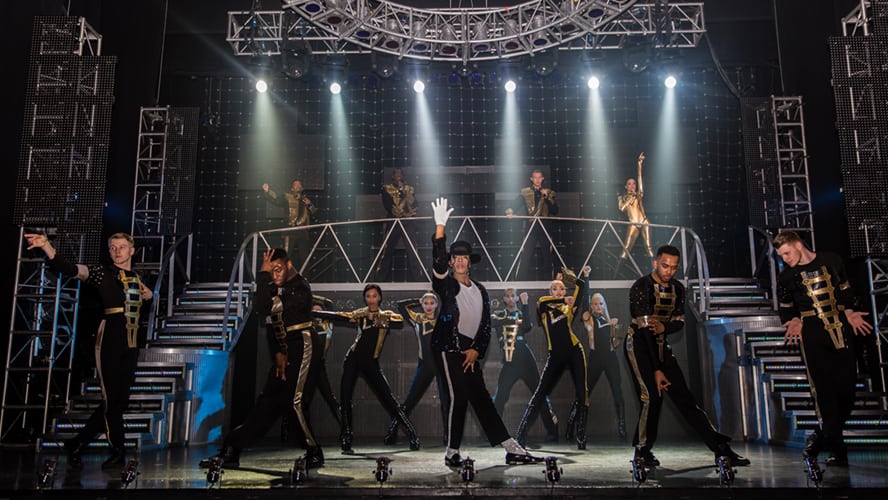 A vibrant stage scene featuring dancers in dynamic poses, illuminated by colourful spotlights.