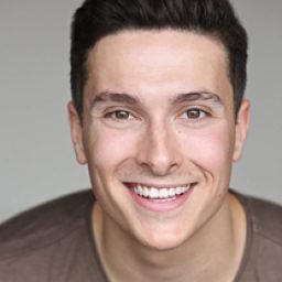 Tom Oliver, a man with short brown hair, wearing a blue shirt and smiling at the camera.