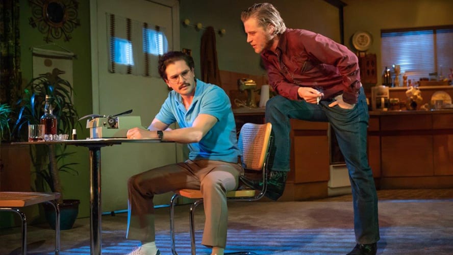 Two actors on stage in a dramatic scene, surrounded by rustic set design and warm lighting.