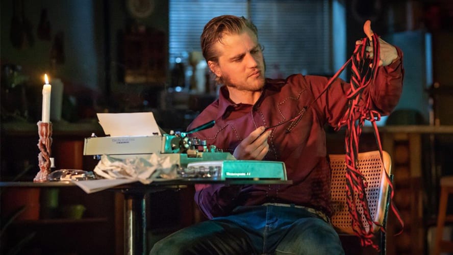 Two actors on stage in a tense confrontation, surrounded by a rustic set design.