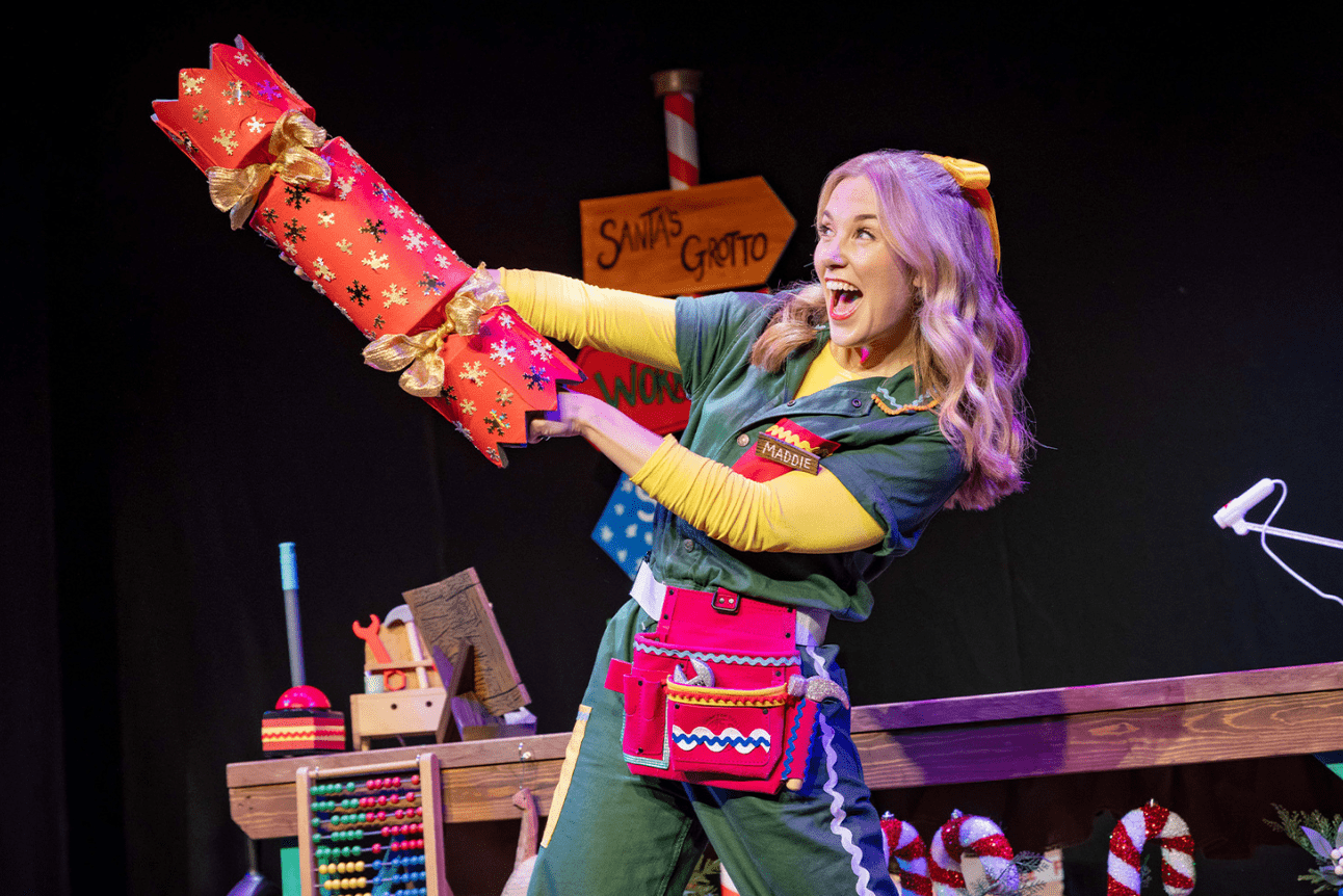 Maddie Moate holding a festive Christmas cracker, smiling in a brightly decorated setting.