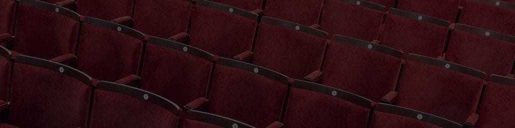 Red velvet seats arranged in rows within a vintage vaudeville auditorium, illuminated by warm lighting.