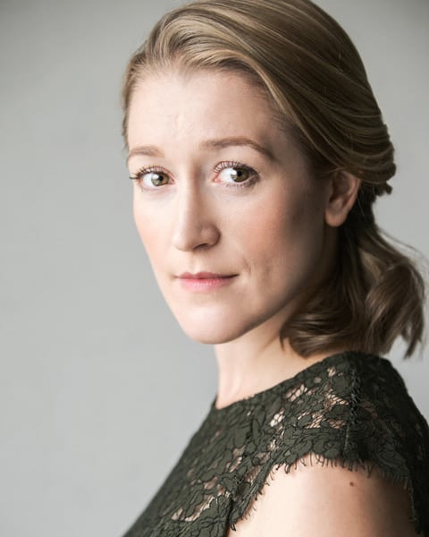 Victoria Blunt smiling, wearing a black blazer and white blouse, with shoulder-length brown hair.