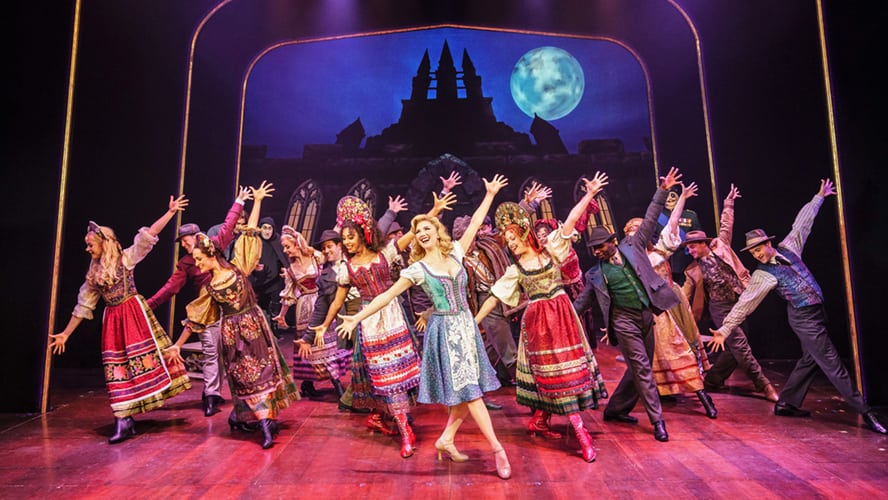 A theatrical scene featuring characters in period costumes, dramatic lighting, and an ornate backdrop.