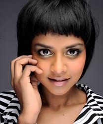 Yshani Perinpanayagam smiling, wearing a blue blouse, with long dark hair and a neutral background.