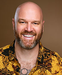 Zachary-James smiling, wearing a blue shirt, with short brown hair and a neutral background.