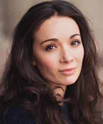 Briony Corrigan smiling, wearing a navy blazer and white blouse, with shoulder-length brown hair.