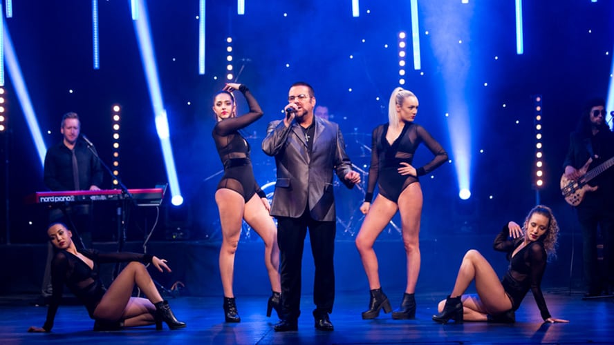 A vibrant stage scene with performers in stylish costumes, bright lights, and an enthusiastic audience.