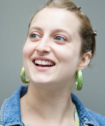 Harriet Braine smiling, wearing a black top, with wavy hair and a neutral background.