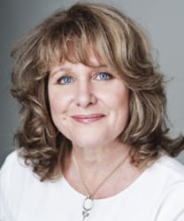 Jan Ravens smiling, wearing a black top, with shoulder-length dark hair and a neutral background.
