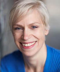 Liv Spencer smiling, wearing a black top, with long brown hair and a blurred background.