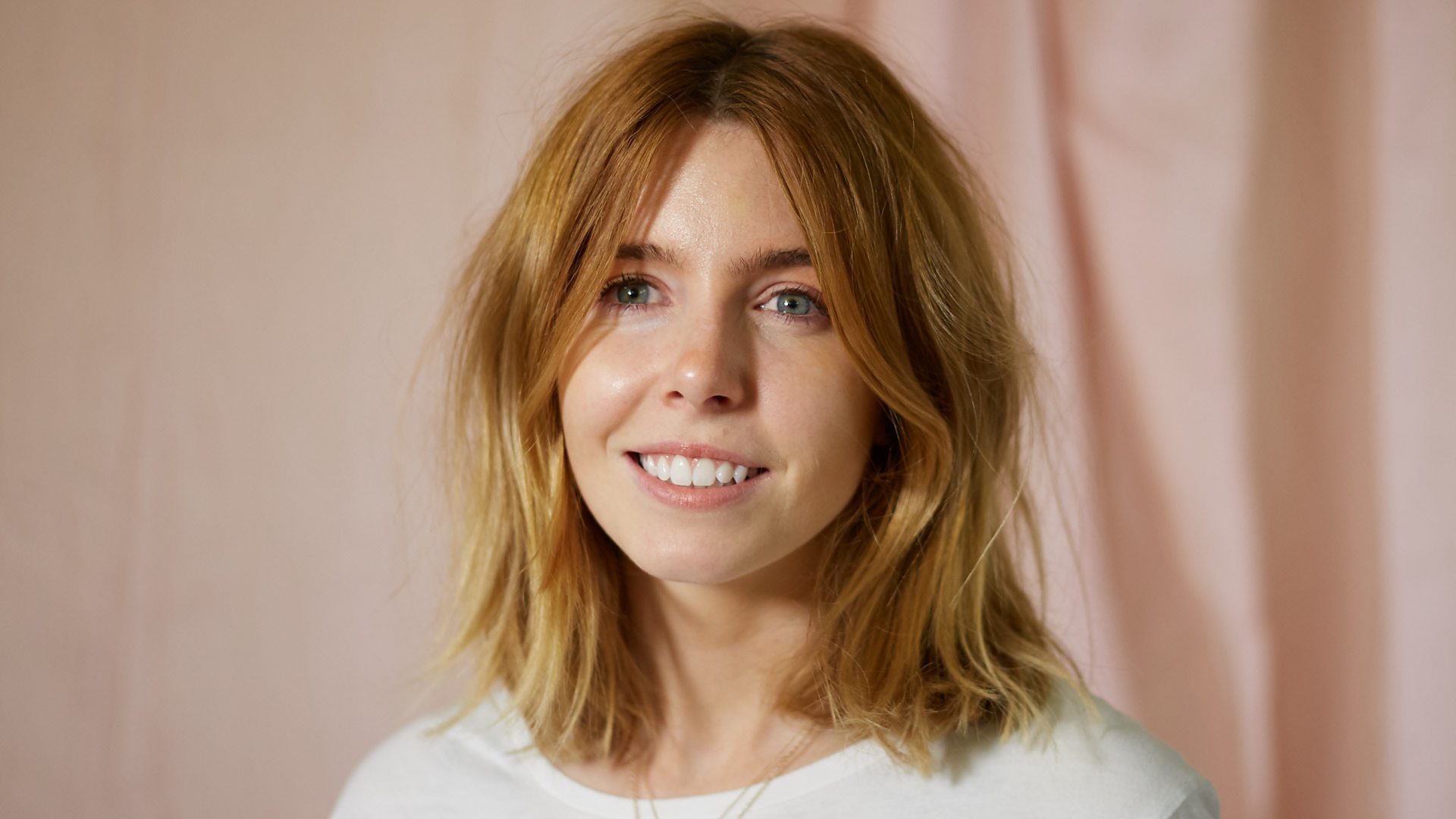 Stacey Dooley speaking on stage, illuminated by soft lighting, with an audience in the background.