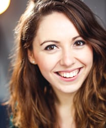 Phoebe Fildes smiling, wearing a black top, with long brown hair and a blurred background.