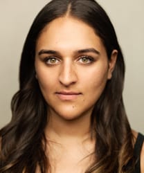 Roxy Faridany smiling, wearing a black blazer and white blouse, with long dark hair.