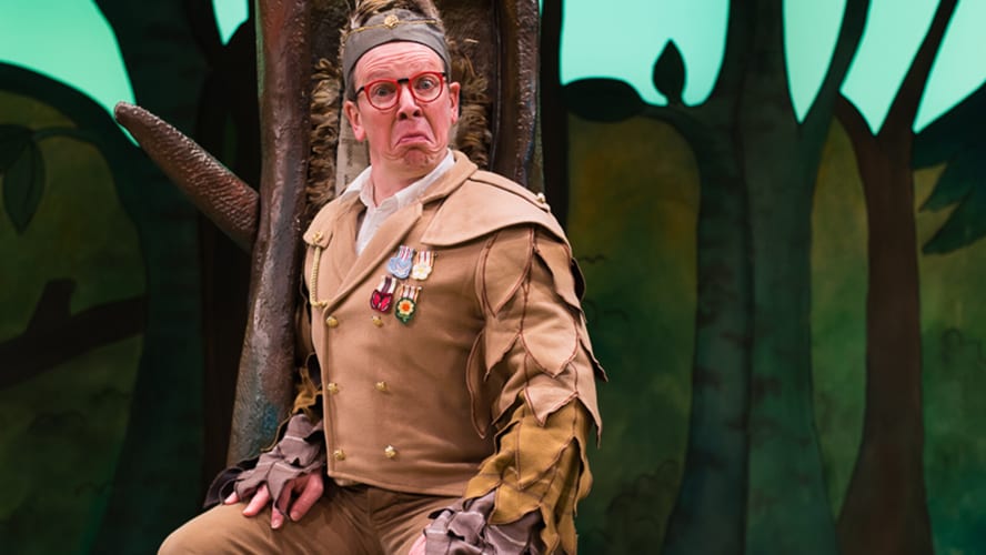 A large, friendly Gruffalo character stands in a forest, surrounded by trees and foliage.