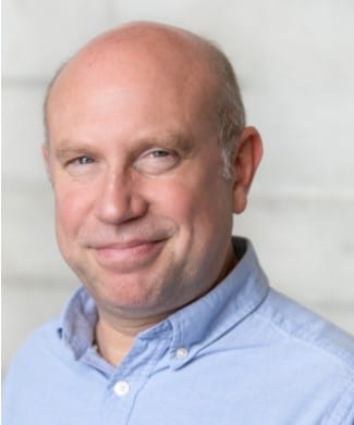 Timothy Speyer, smiling man with short dark hair, wearing a blue shirt and blazer.