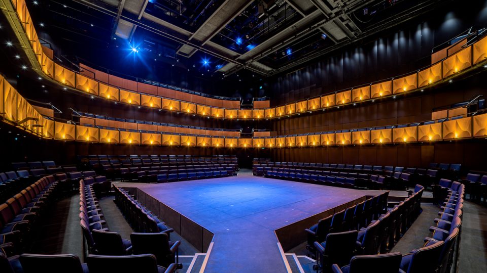 A modern theatre interior featuring plush seating, elegant lighting, and a spacious stage area.