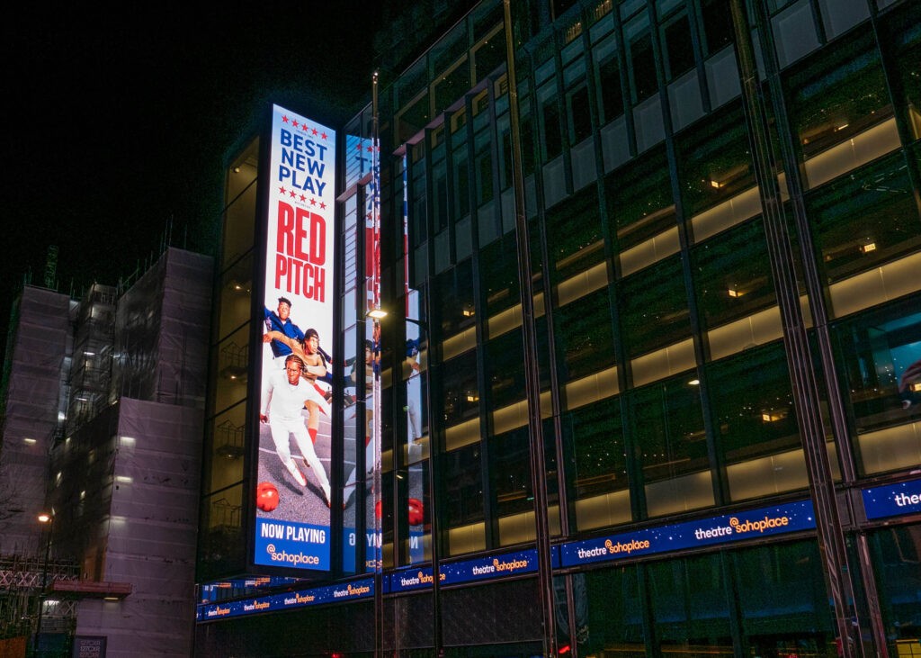 Bright red poster displayed outside Soho Place, featuring bold text and graphics.