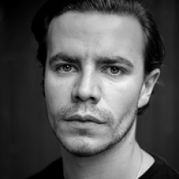 Black and white portrait of Oliver Johnstone, featuring a thoughtful expression and soft lighting.