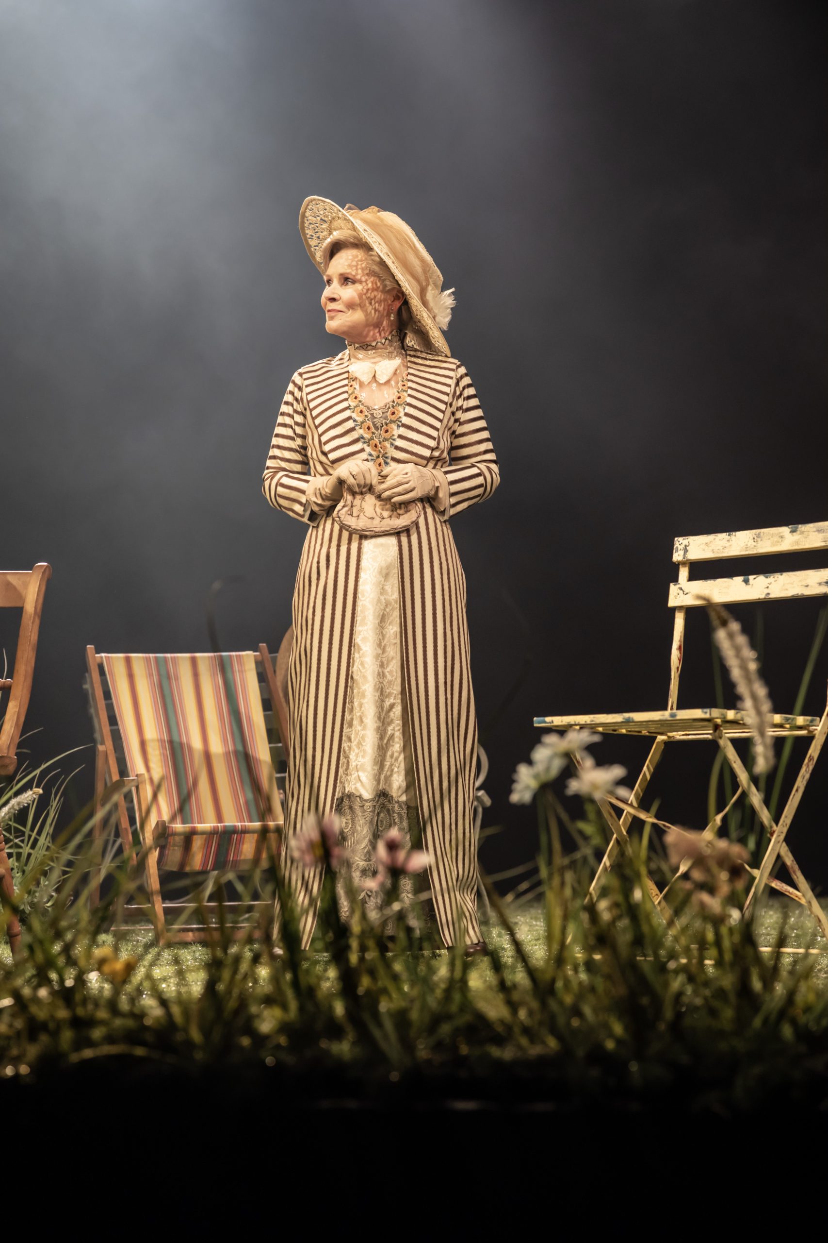 A theatrical scene featuring two women in period costumes, engaged in conversation on a stage.