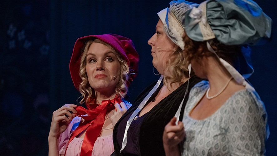 Austentatious performance scene featuring actors in period costumes, set in a theatre with audience.