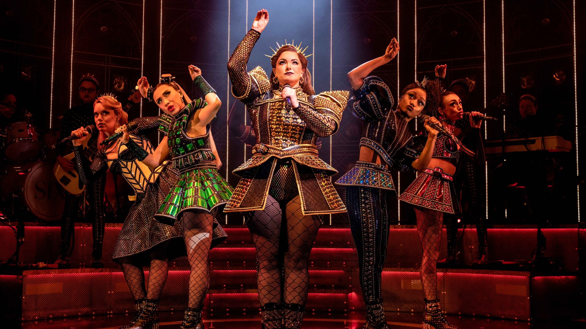 SIX H Nikki Bentley as Aragon, surrounded by the cast of SIX the Musical, on stage.
