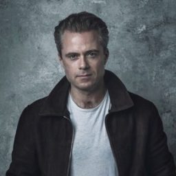 Rory Keenan as a character in The Spy Who Came In From The Cold, wearing a dark suit.