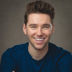 Headshot of Alex Lodge, featuring a smiling expression and neatly styled hair against a neutral background.