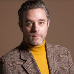 Andy Nyman as Max Bialystock, wearing a suit and tie, with a theatrical backdrop.