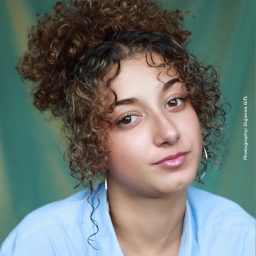 Sabrina with dark hair, smiling, wearing a green top against a neutral background.