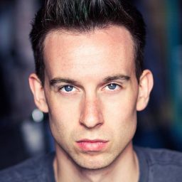 Josh Kiernan performing on stage in a theatrical costume, with dramatic lighting and a vibrant backdrop.