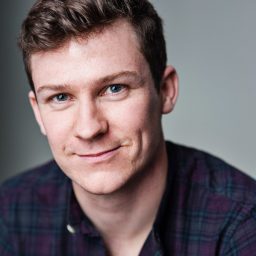 Matt Cavendish, smiling, with short brown hair and a dark suit against a neutral background.