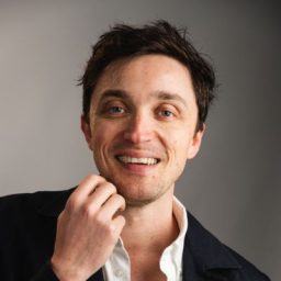 Harry with a friendly smile, wearing a blue shirt against a neutral background.