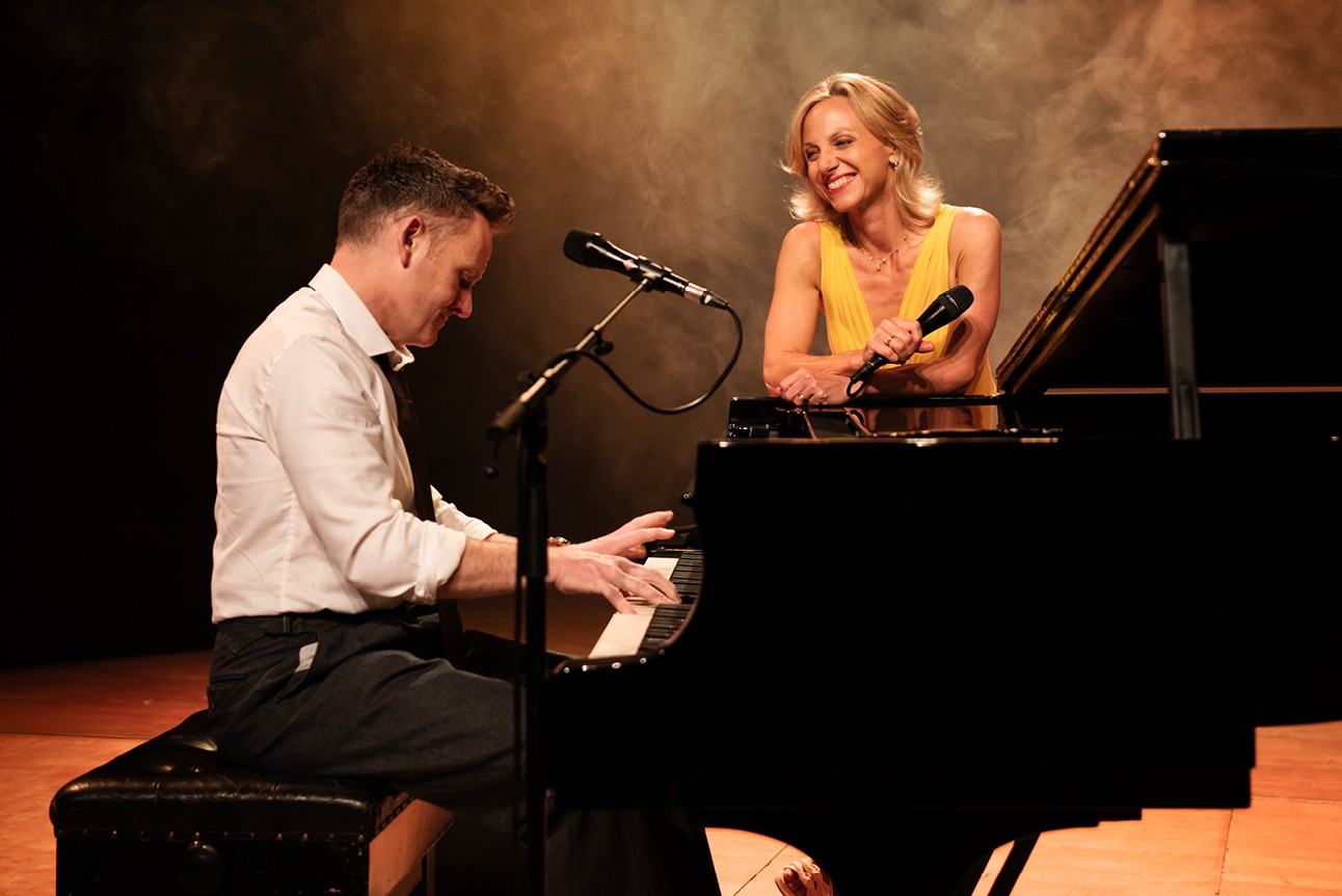 Liza Pulman and Joe Stilgoe perform on stage, surrounded by vibrant lights and a cheering audience.