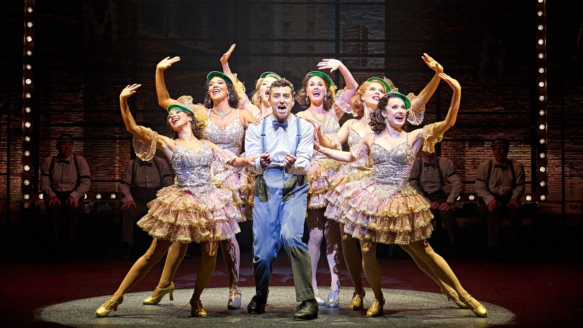 The Producers Marc Antolin as Leo Bloom, surrounded by a diverse ensemble cast in theatrical costumes.