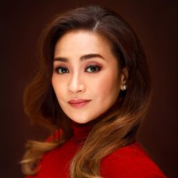 Joanna Ampil smiling, wearing a stylish outfit, with a softly lit background at the event.