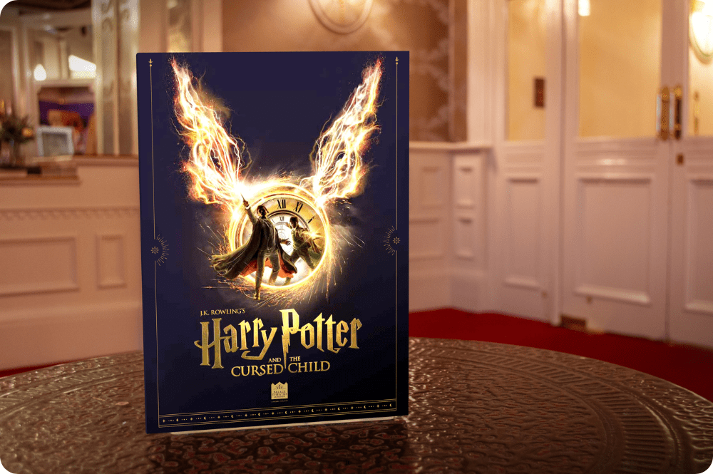 Harry Potter and the Cursed Child theatre programme with fiery wings design on dark blue cover, placed on a table.