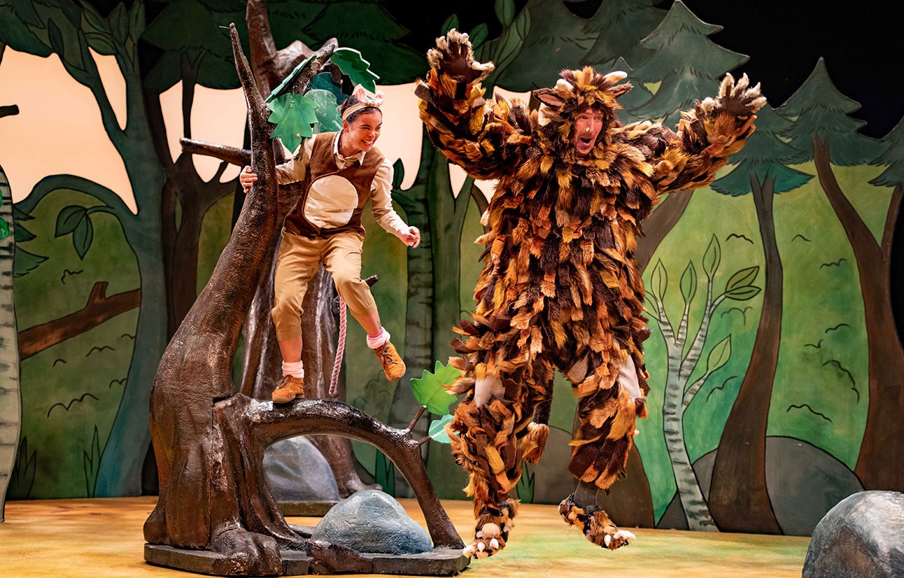 Two actors in detailed Gruffalo costumes perform energetically on a colourful forest-themed stage set.