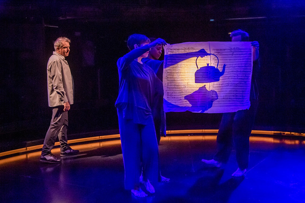 Phelim McDermott, Sarah Wright, Janet Etuk, and David Emmings perform under blue lighting, holding a translucent screen.